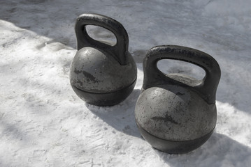 Two old black heavy kettlebell stand on the snow. Before the practice of weightlifting in the winter in the fresh air