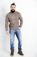 Fashion portrait of young stylish bearded man in trendy casual sweater and blue jeans and leather boots over white background.