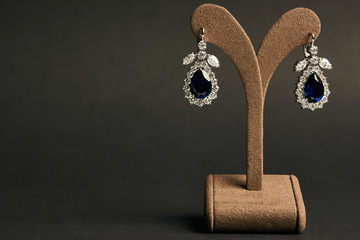 Close up diamond earrings with blue sapphire on dark background with copy space. Luxury female...