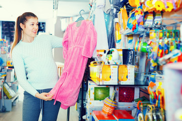 Pregnant woman is choosing baby clothes in the shop.