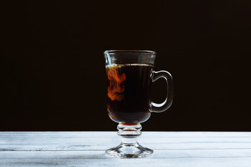 Pouring milk in glass of hot coffee over dark background, for banner, free copyspace for text. Coffee shop concept.
