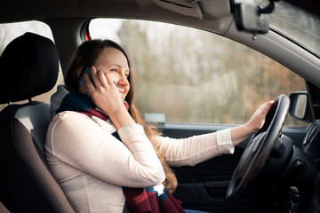 Pretty young brunette woman calling during driving car, using smartphone in the car