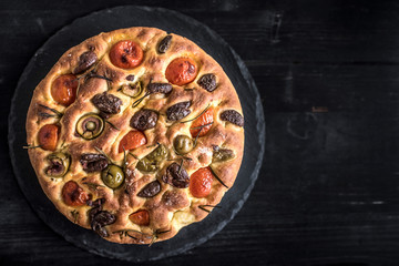 Homemade Italian Focaccia bread with olives and tomatoes on dark background with blank space