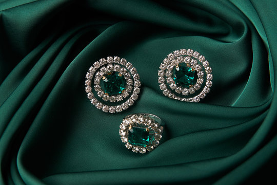 Diamond ring and earrings with emerald on a green silk background. Luxury female jewelry, close-up
