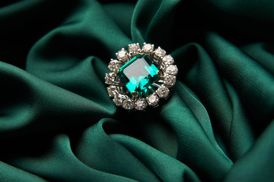 Diamond ring and earrings with emerald on a green silk background. Luxury female jewelry, close-up