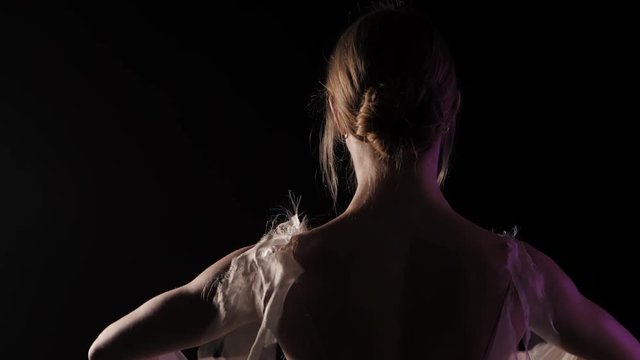 Ballerina is practicing her moves in dark studio. Young girl dancing with air white dress tutu, spinning around and smiling. Gracefulness and tenderness in every movement