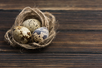 Rustic still life - quail eggs in nest on wood background, close-up with place for text, Easter style