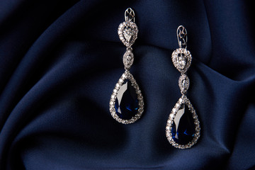 Pair of platinum earring with sapphire on blue satin background. Luxury female jewelry, close-up