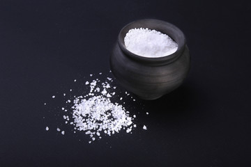 White sea salt in clay bowl isolated on a black background. Selective focus.