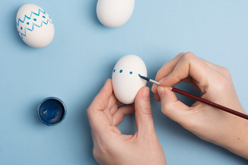 Holidays, tradition and people concept - close up of woman hands coloring easter eggs with brush