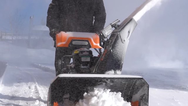 The man is removing snow with a snow blower in a blizzard.