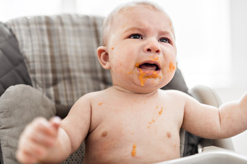 Messy and dirty baby is eating snack and crying.