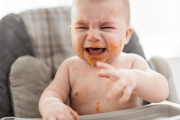 Messy and dirty baby is eating snack and crying.