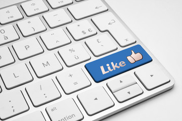Like blue button with a thumb up icon on a white isolated keyboard - social media concept