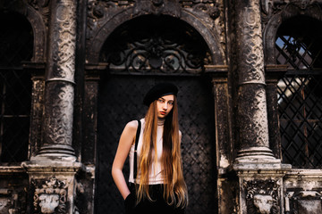 A stylishly dressed girl with long hair standing on the back of the house with ancient columns and metal doors