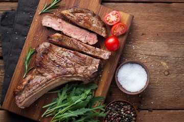 Grilled cowboy beef steak, herbs and spices on a rustic wooden background. Top view with copy space...