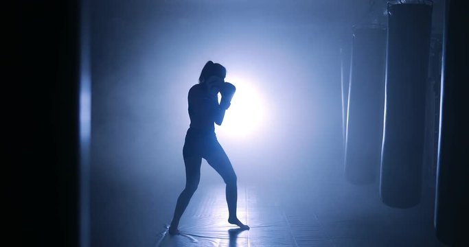 Woman sportsman boxing in smoky studio. Silhouette on a dark background