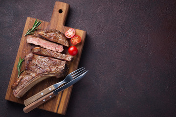 Grilled cowboy beef steak, herbs and spices on a dark stone background. Top view with copy space...