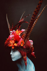 Mannequin in creative headwear with flowers and feathers against dark background