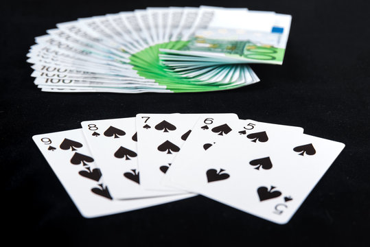 Fan of one hundred euro banknotes money on casino poker with straight flush cards on black background