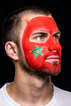 Portrait of handsome man face supporter fan of Morocco national team with painted flag face isolated on black background. Fans emotions.