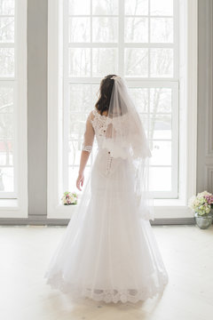 bride is staying near the window in wedding dress and veil closeup