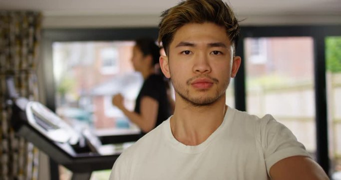 4K Young Asian man working out with dumbbells at the gym & girl running on treadmill in background. Slow motion.