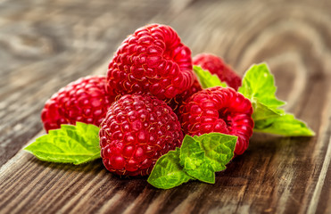 Ripe fresh raspberries with leaves on a wooden background