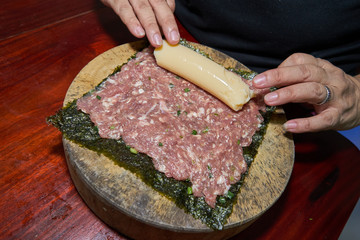 Woman hands to handle pork marinated tofu wrapped eggs on kelp on a wooden cutting board on a wooden table