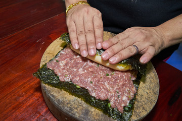 Woman hands to handle pork marinated tofu wrapped eggs on kelp on a wooden cutting board on a wooden table