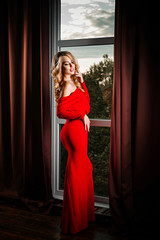 Luxurious woman in red dress posing in the room