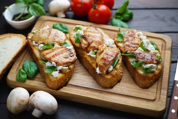 Fototapeta na wymiar Traditional Italian antipasti bruschetta with grilled chicken, ricotta and basil on wooden board, close up. Appetizing food background