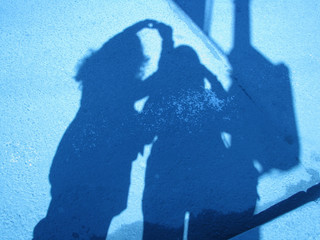 Two girls making selfy blue shape shadows on stucco wall