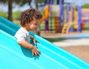 Young boy with curly hair has fun as he goes down a slide at a playground.