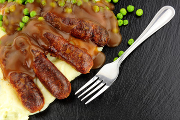 Sausages and mashed potato meal with garden peas on a slate background
