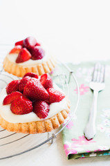 Strawberry tartlets with genoise sponge cake base and French vanilla custard pudding, called creme patissiere, for birthday or garden party on white wooden table