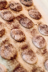 Freshly baked, imperfect and cracked French Macaron shells without feet with chocolate coffee flavor dusted with cocoa powder on silicone mat at baking workshop in France