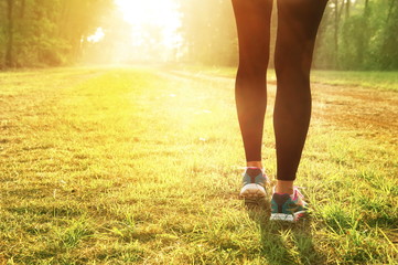 leg of woman with running or training sport shoes with summer morning light green garden outdoor background