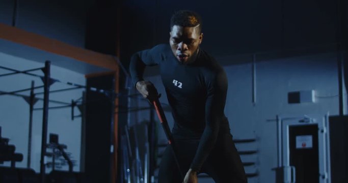 Man exercising with hammer while having crossfit training at gym then falls on the wheel tired. Slow motion 4K shot on Red cinema camera.