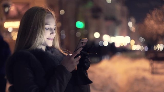 Woman use of smart phone in the winter time at night and smile