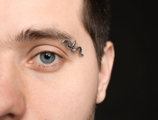Fototapeta premium Young man with pierced eyebrow on black background, closeup