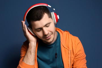 Young man with pierced eyebrow listening to music on color background