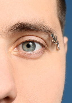 Young man with pierced eyebrow on color background, closeup
