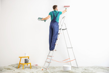 Fototapeta premium Young male decorator painting wall in empty room