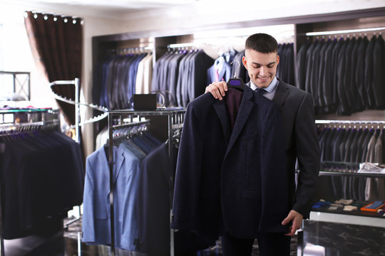 Young man choosing elegant suit in boutique