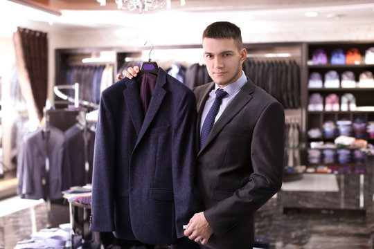 Young man choosing elegant suit in boutique