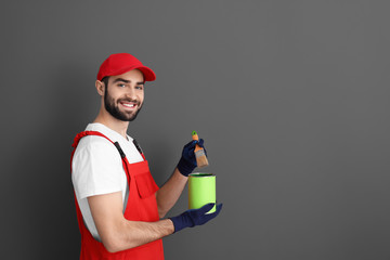 Male decorator holding brush and paint can on grey background