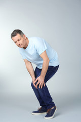 Man suffering from knee pain on light background
