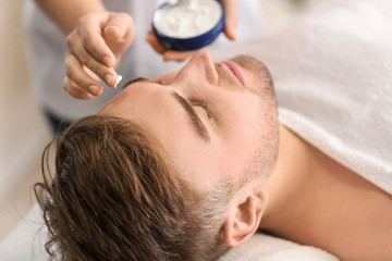 Obraz na płótnie Canvas Beautician applying cream on young man's face in spa salon