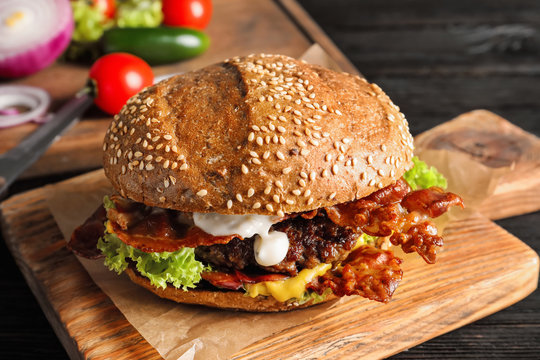 Tasty burger with bacon on wooden board